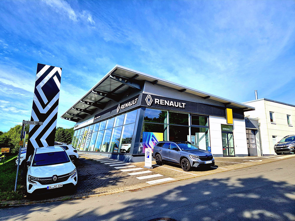 Automobile Clever E-Tech Außenansicht des Renault-Autohauses der Familie Clever mit ausgestellten Fahrzeugen, großem Renault-Logo und markanter schwarz-weißer Werbefahne.