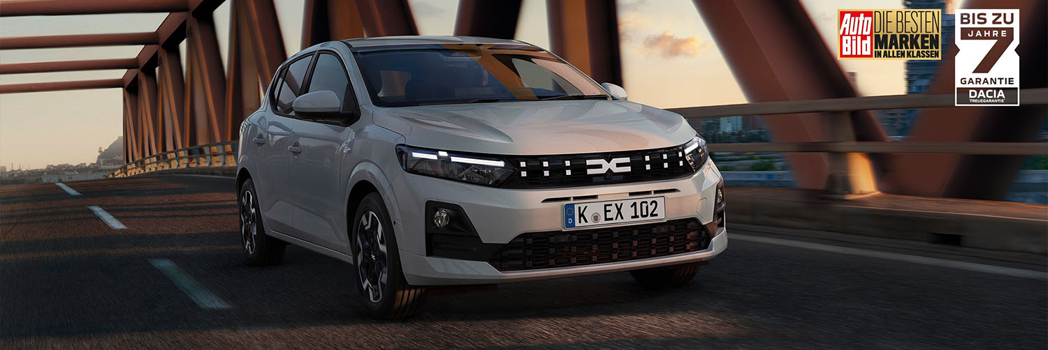 Ein aktueller Dacia Sandero in elegantem Grau bei der Überquerung einer markanten roten Stahlbrücke.